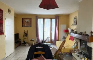 Un salon aux murs jaunes, un canap&eacute; recouvert d'un jet&eacute; jaune, une chemin&eacute;e sur la droite et de grandes fen&ecirc;tres aux rideaux diaphanes laissant entrer une lumi&egrave;re douce : cet ancien s&eacute;jour avant r&eacute;novation d&eacute;gage un aspect vieillot avant d'&ecirc;tre remis au go&ucirc;t du jour.